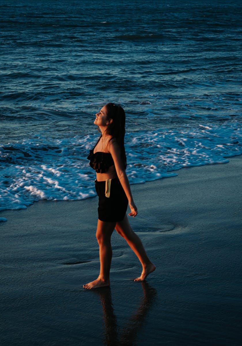 A young woman walks barefoot along the beach in Santa Marta, Colombia, enjoying a serene sunset.